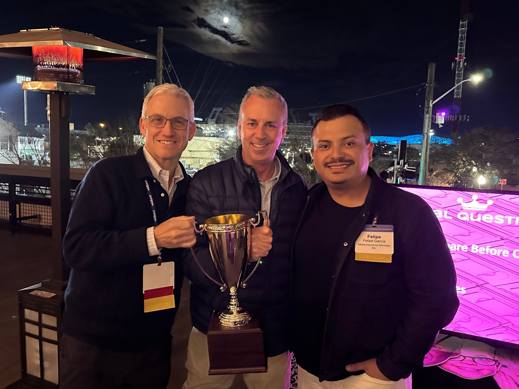 Three guests holding the Trivia Nation trophy on a rooftop terrace at night